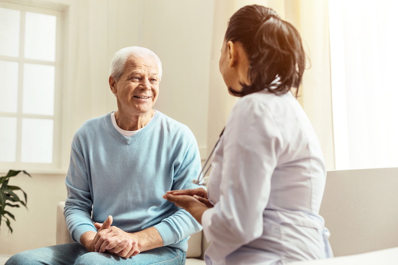 Positive cheerful senior man smiling and looking at the nurse while having a conversation with her
